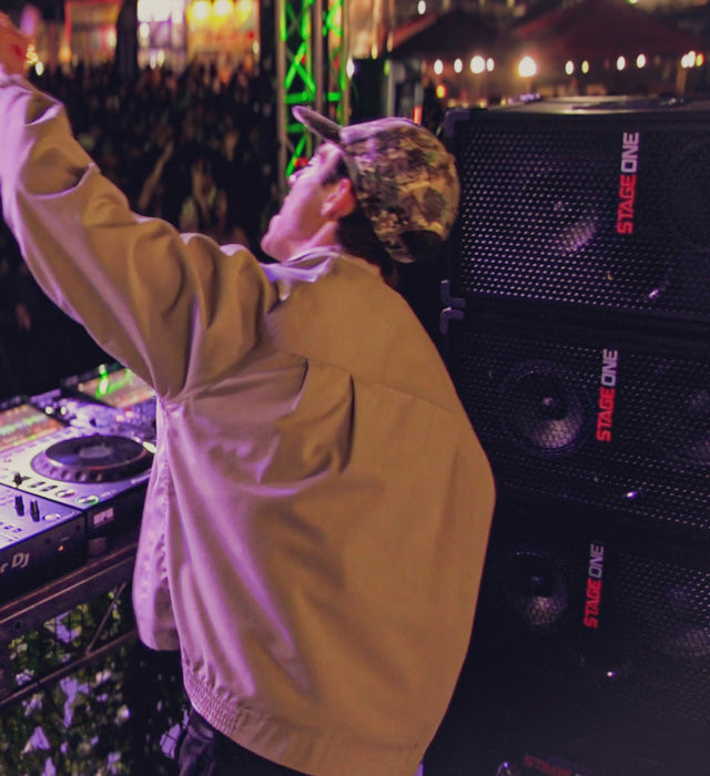 DJ at a concert with Stage One speakers and crowd in the background